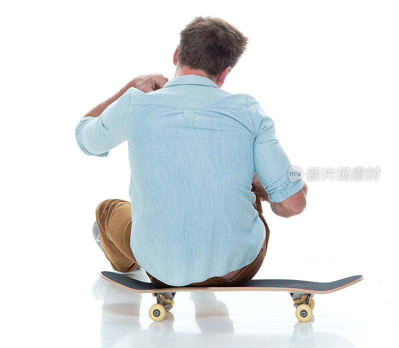 全长/一人/后视图20-29岁英俊的人/短发白人男性/年轻男子滑板/滑板/滑冰/坐在地板上，在前面的白色背景穿着纽扣衬衫/裤子